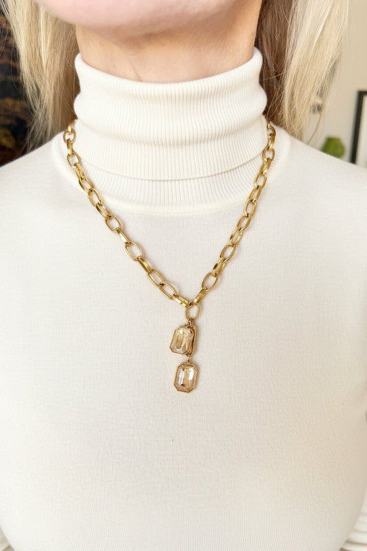 a woman in an ivory tutleneck sweater wearing a gold pendant necklace in an interior setting