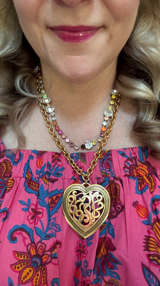 Up close view of a woman wearing a large gold filigree heart necklace and pink floral dress