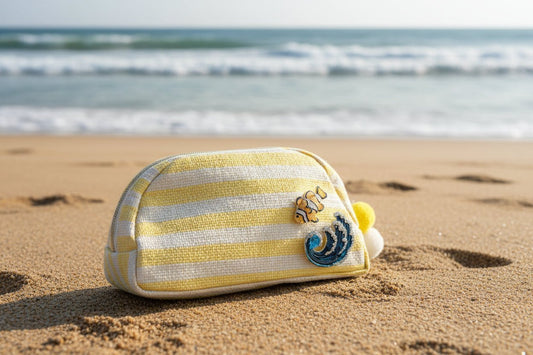 A yellow and beige striped pouch with ocean themed brooches in the sand with the ocean in the background