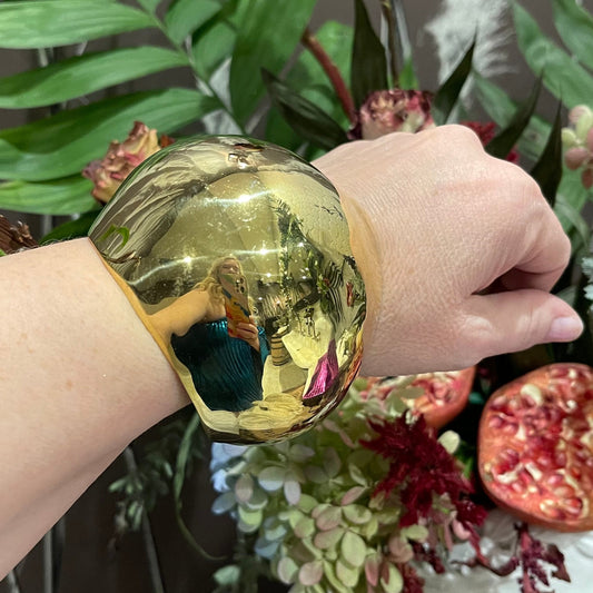 a woman's arm with a brass dome cuff bracelet against a floral arrangement background