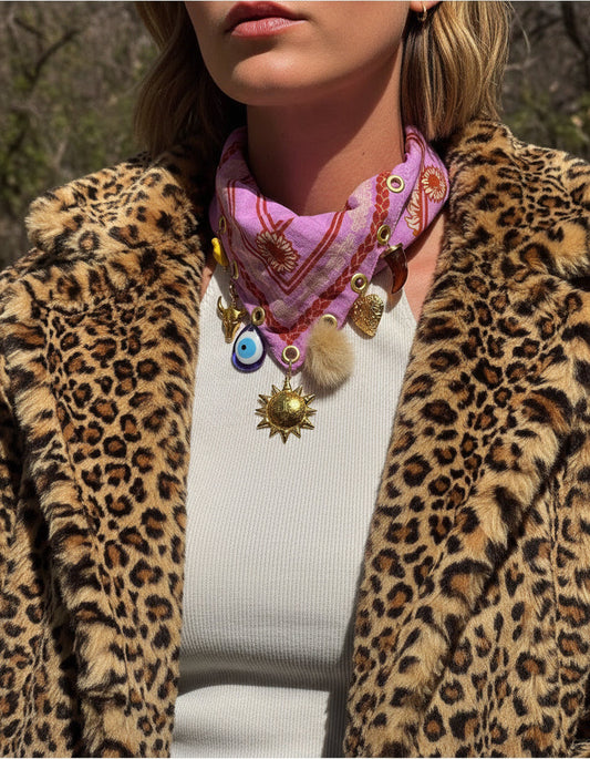A woman in a leopard faux fur coat and pink bandana scarf with various charms in an outdoor setting