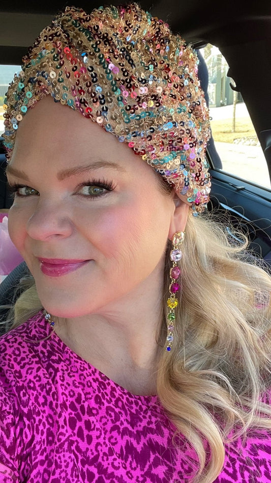 A woman in a pink dress and sequin turban wearing rainbow crystal drop earrings in her car