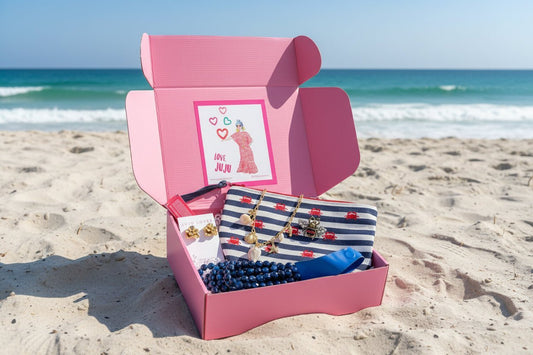 A pink curated gift box full of accessories from JuJu Loves on the beach with the ocean in the background