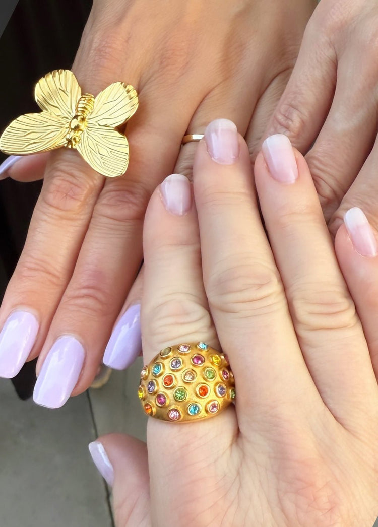 two hands wearing a gold butterfly ring and a multi stone gold ring