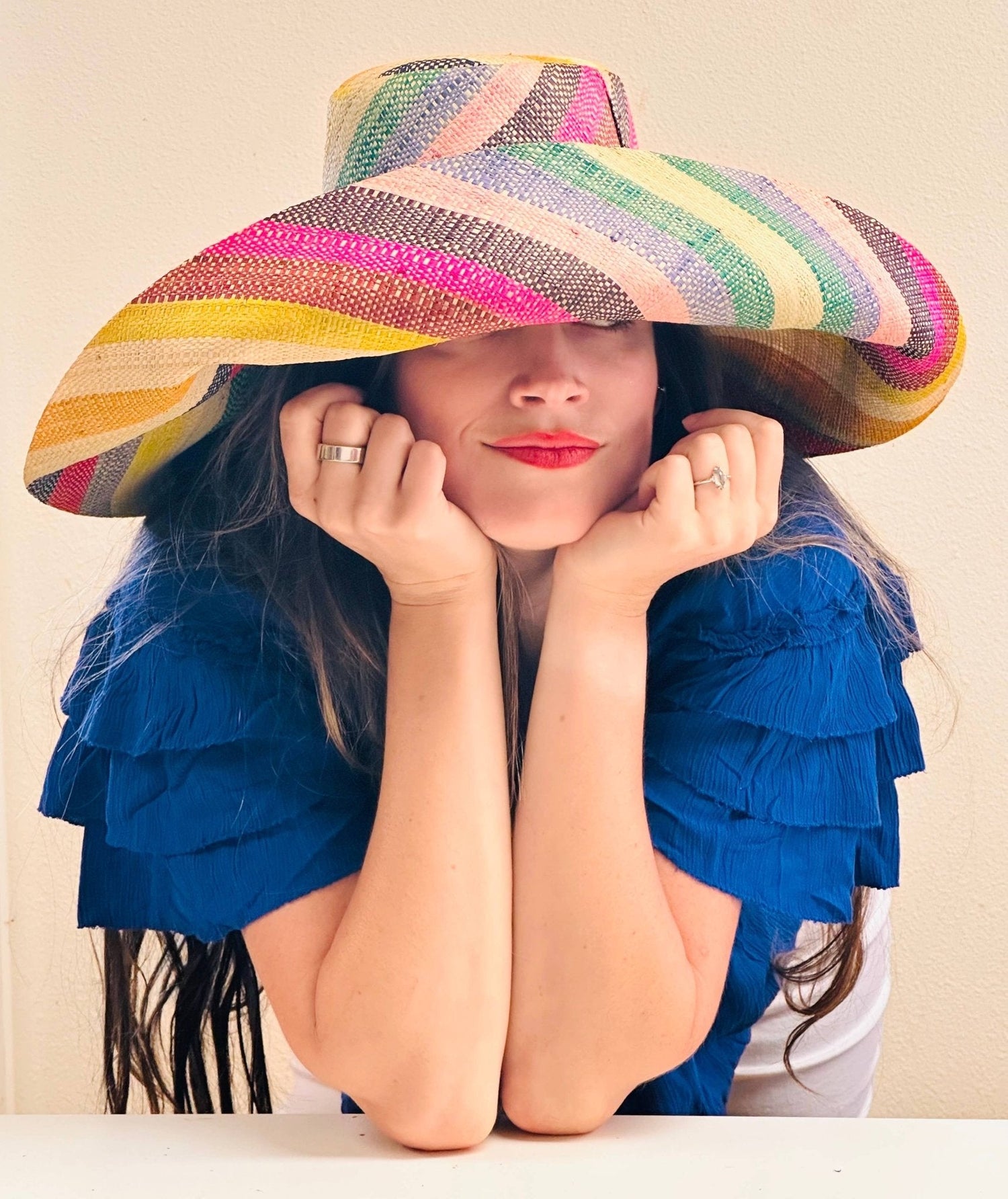 A woman wearing a multi colored striped sun hat with a neutral background