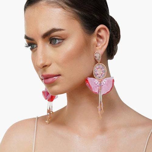 A woman wearing pink flower and beaded drop earrings against a white background