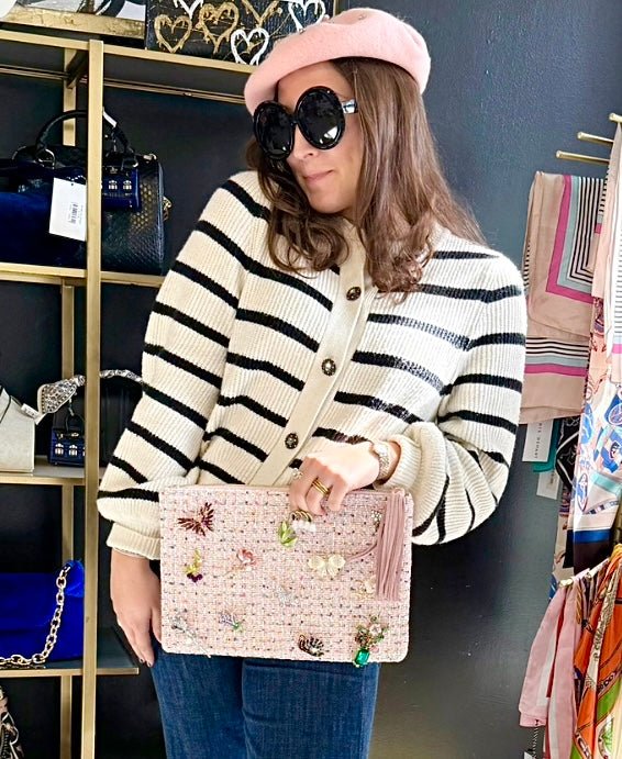 woman in a pink beret holding a pink tweed clutch with multiple brooches in an indoor setting