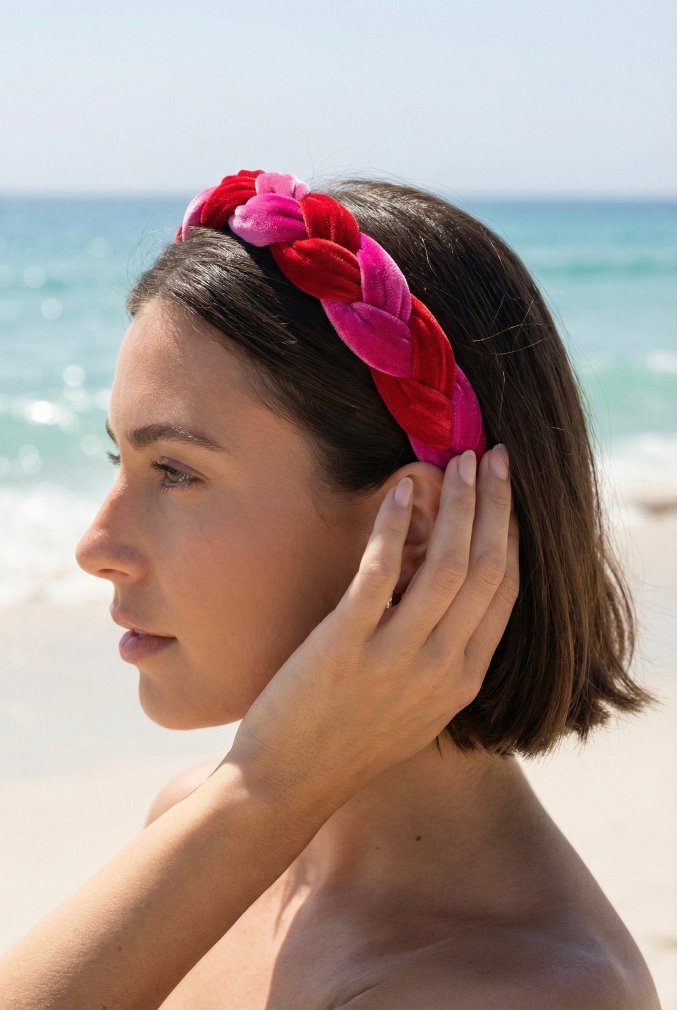 Woman on a beach wearing a red and pink braided headband with ocean in the background
