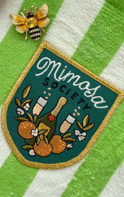 Patch with 'Mimosa Society' design and a yellow bee brooch on a green and white striped background