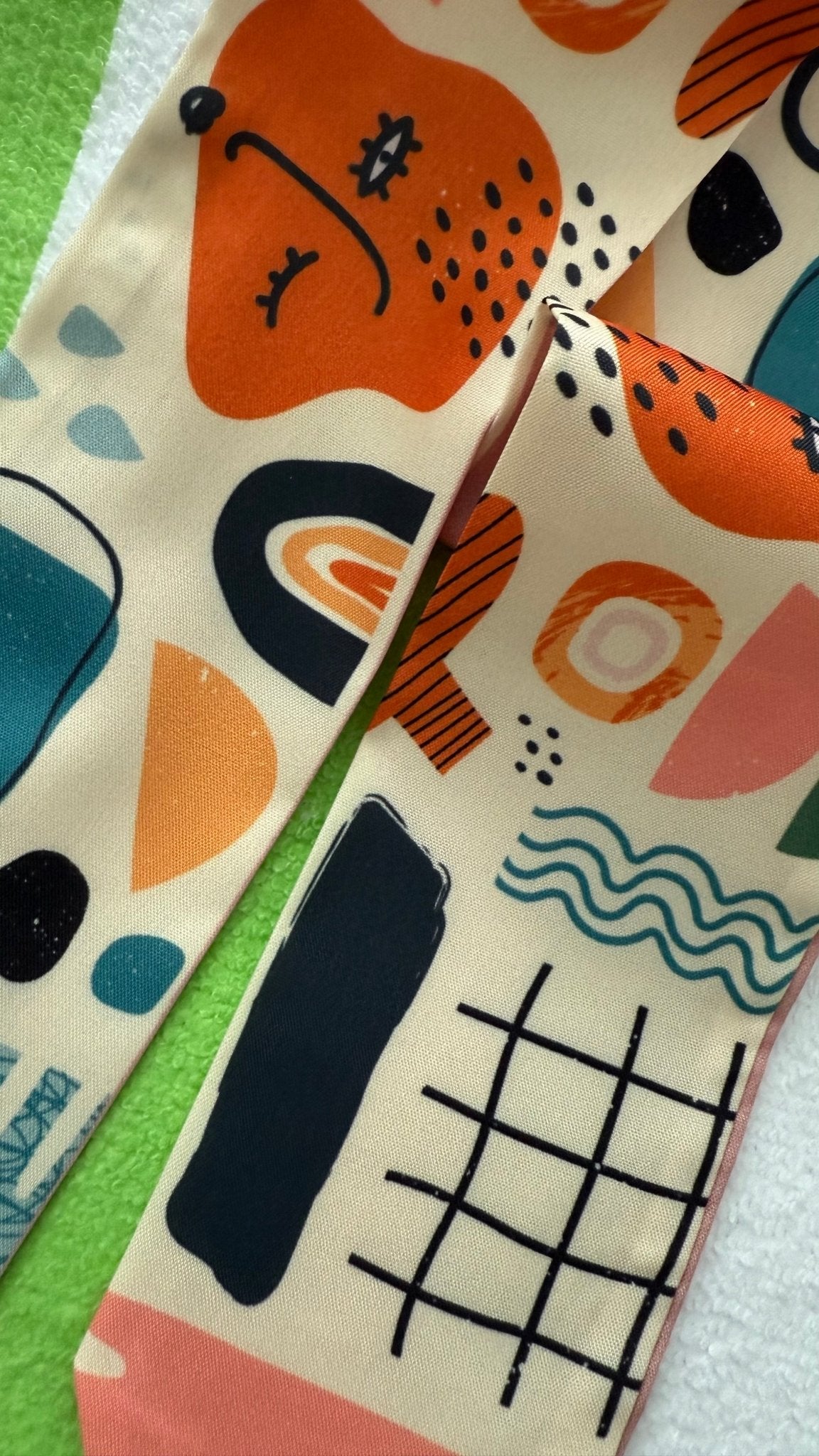 Up close view of colorful twilly scarf fabric with abstract shapes and patterns on a green and white background