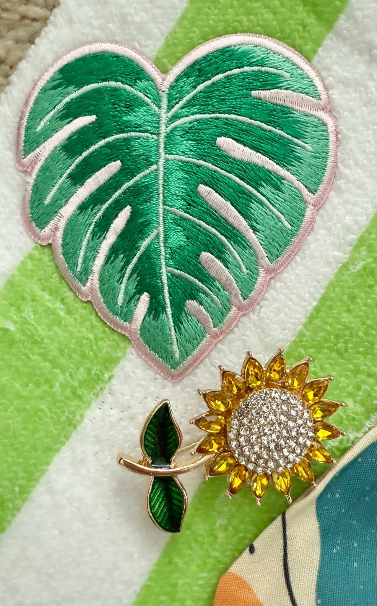 Decorative sunflower brooch and palm leaf patch on a green and white striped background