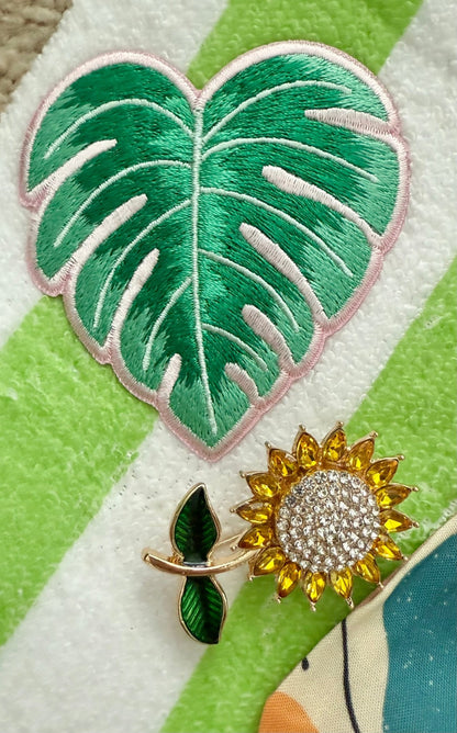 Decorative sunflower brooch and palm leaf patch on a green and white striped background