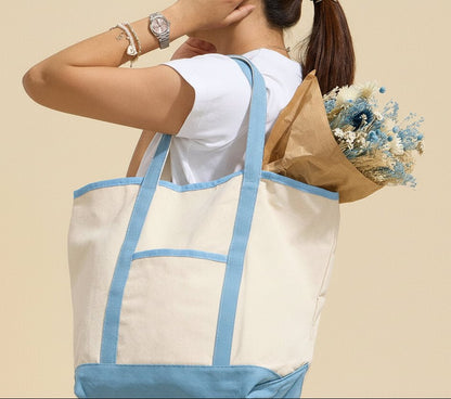 Person holding a large tote bag with light blue trim on a beige background