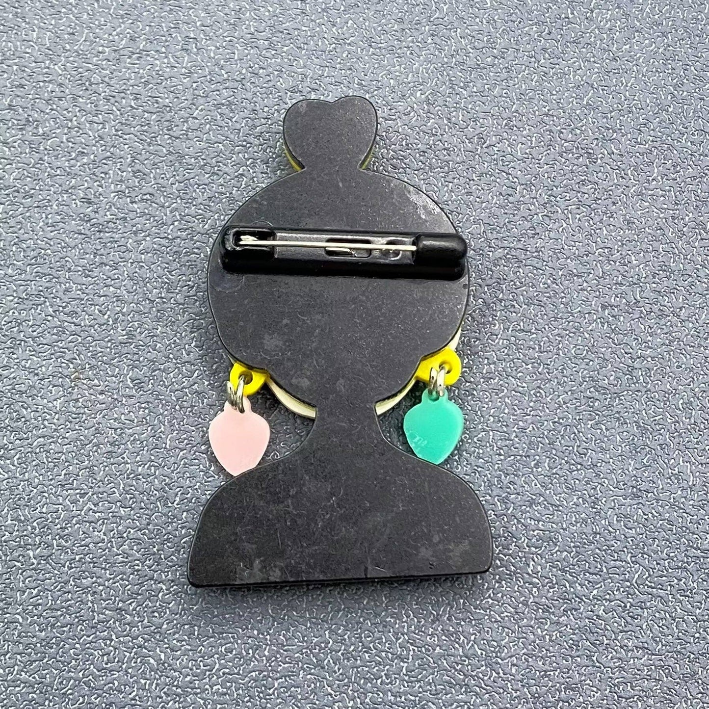 back view of fashionista brooch showing pin closure against textured grey background