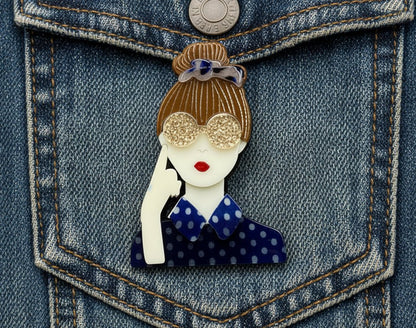Fashionista brooch of woman with hand next to face against a denim jacket background