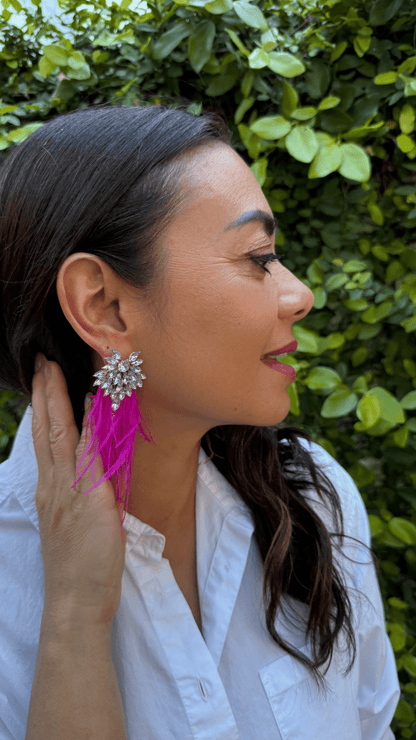 Woman wearing a white shirt and pink fuchsia feather earrings with a blurred green background