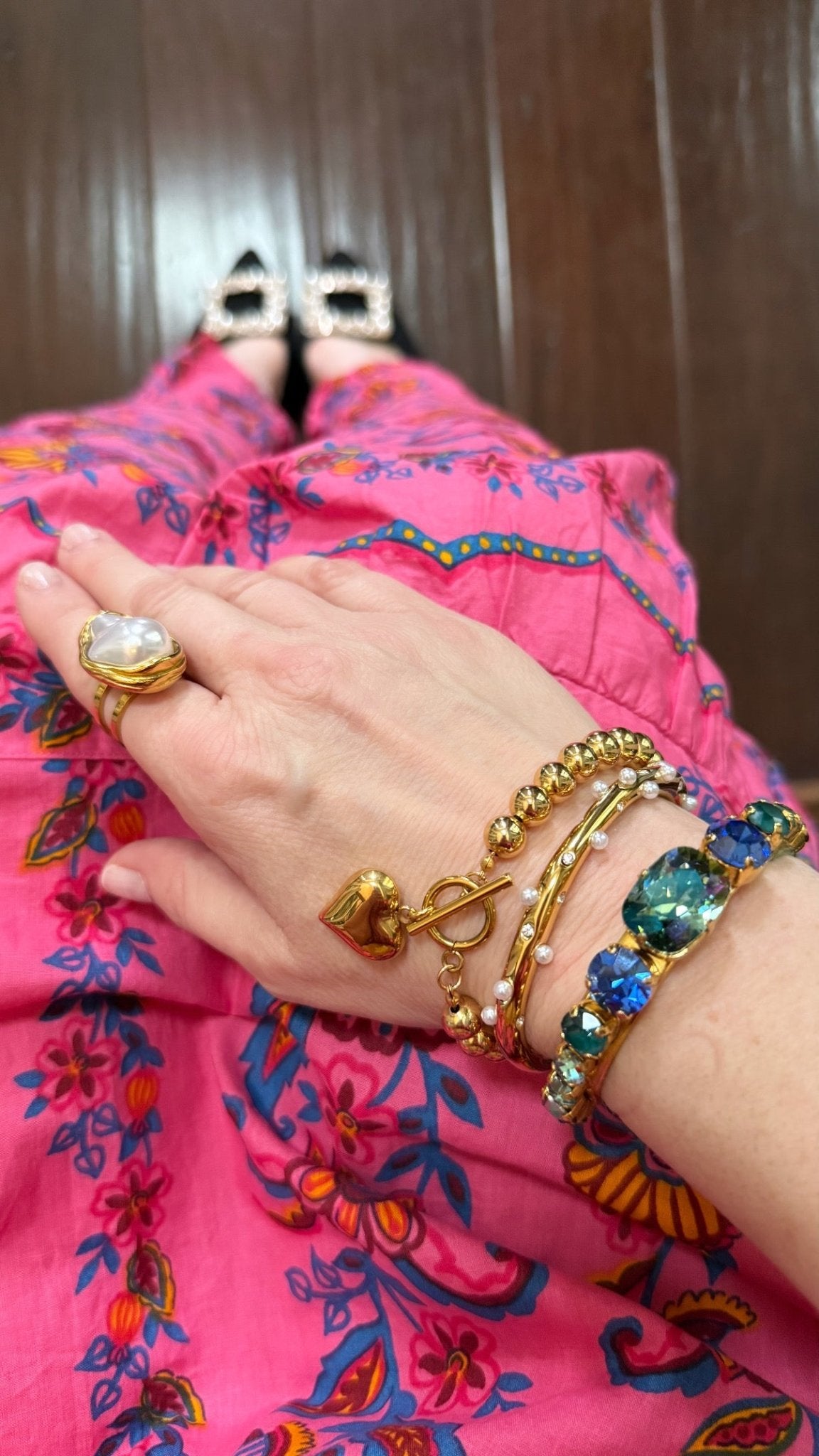 Close-up of a hand wearing colorful bracelets and a pearl ring on a pink patterned fabric background