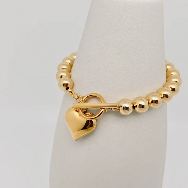 Gold puffy heart charm bead bracelet with toggle clasp on white background