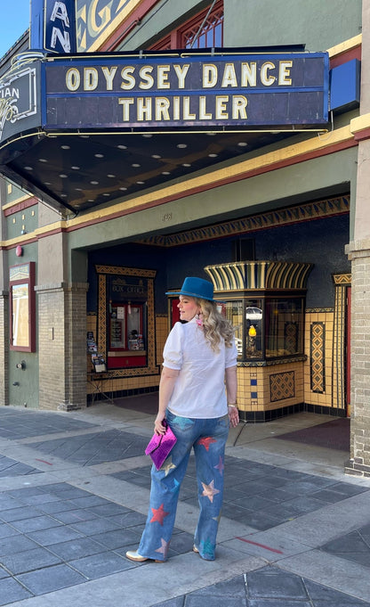 A woman standing in front of a theater with 'Odyssey Dance' and 'Thriller' marquee wearing star rhinestone embellished jeans