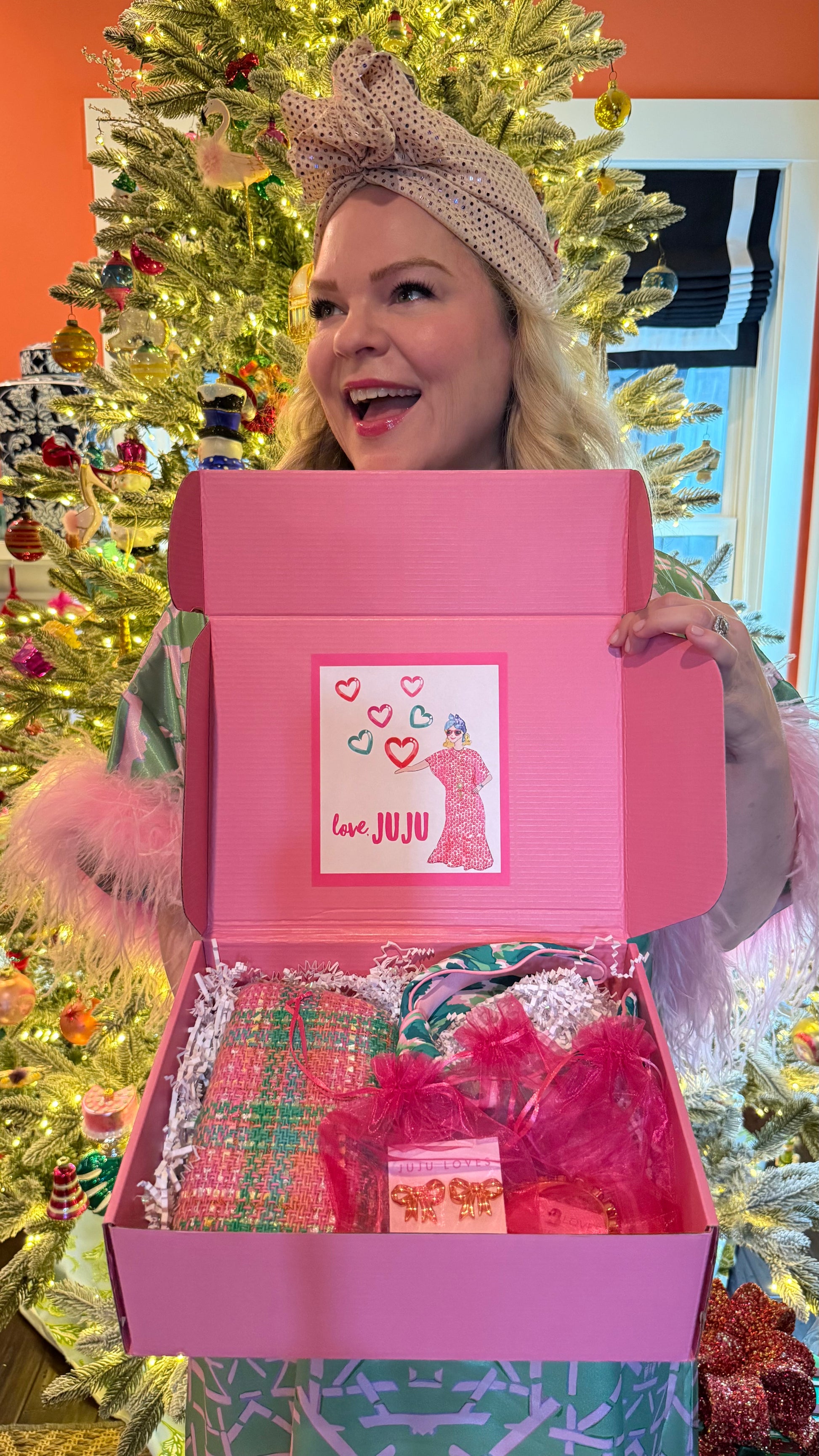 Person holding a pink gift box with a Christmas tree in the background