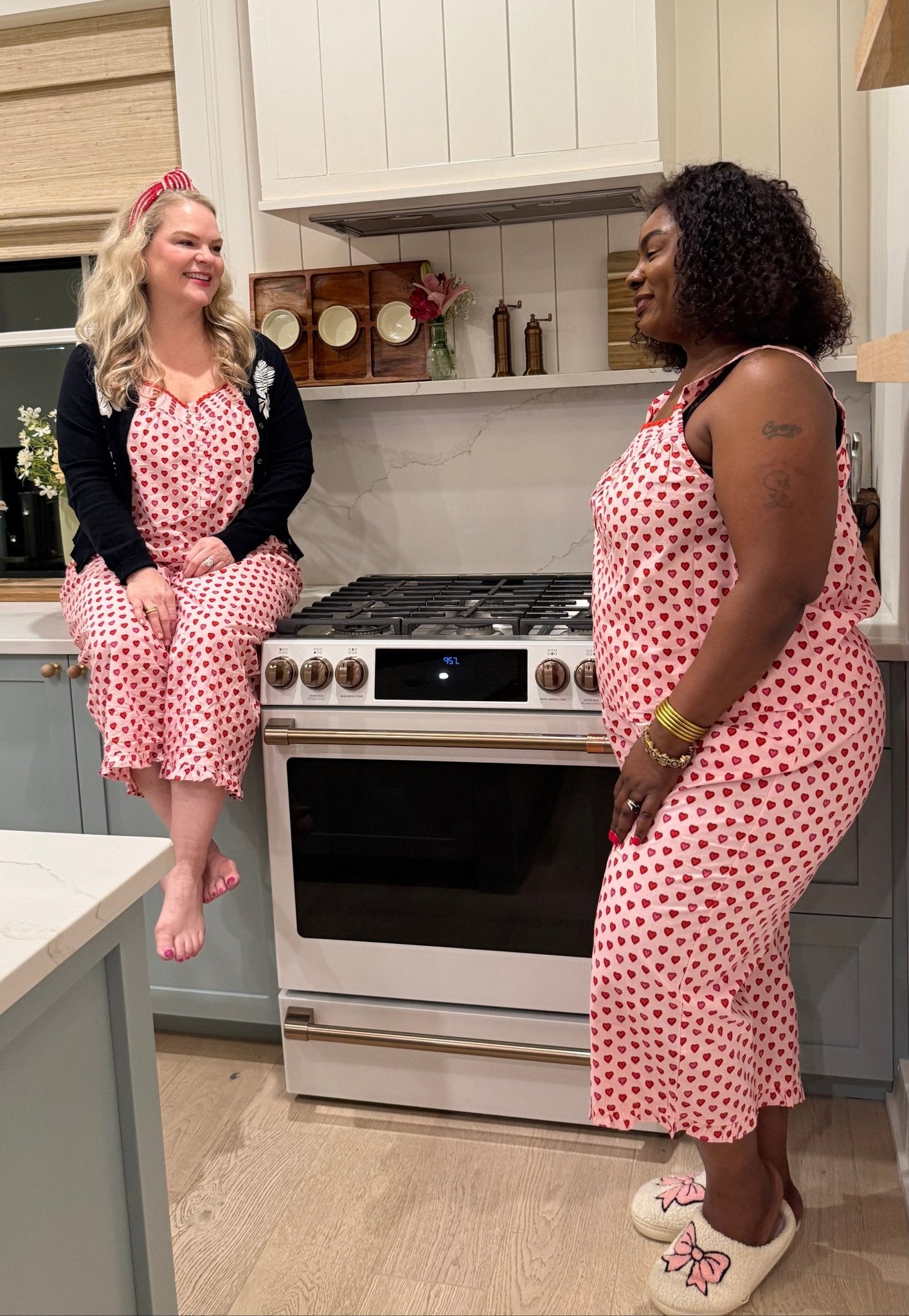 Two women in matching pink polka dot pajamas standing in a kitchen.