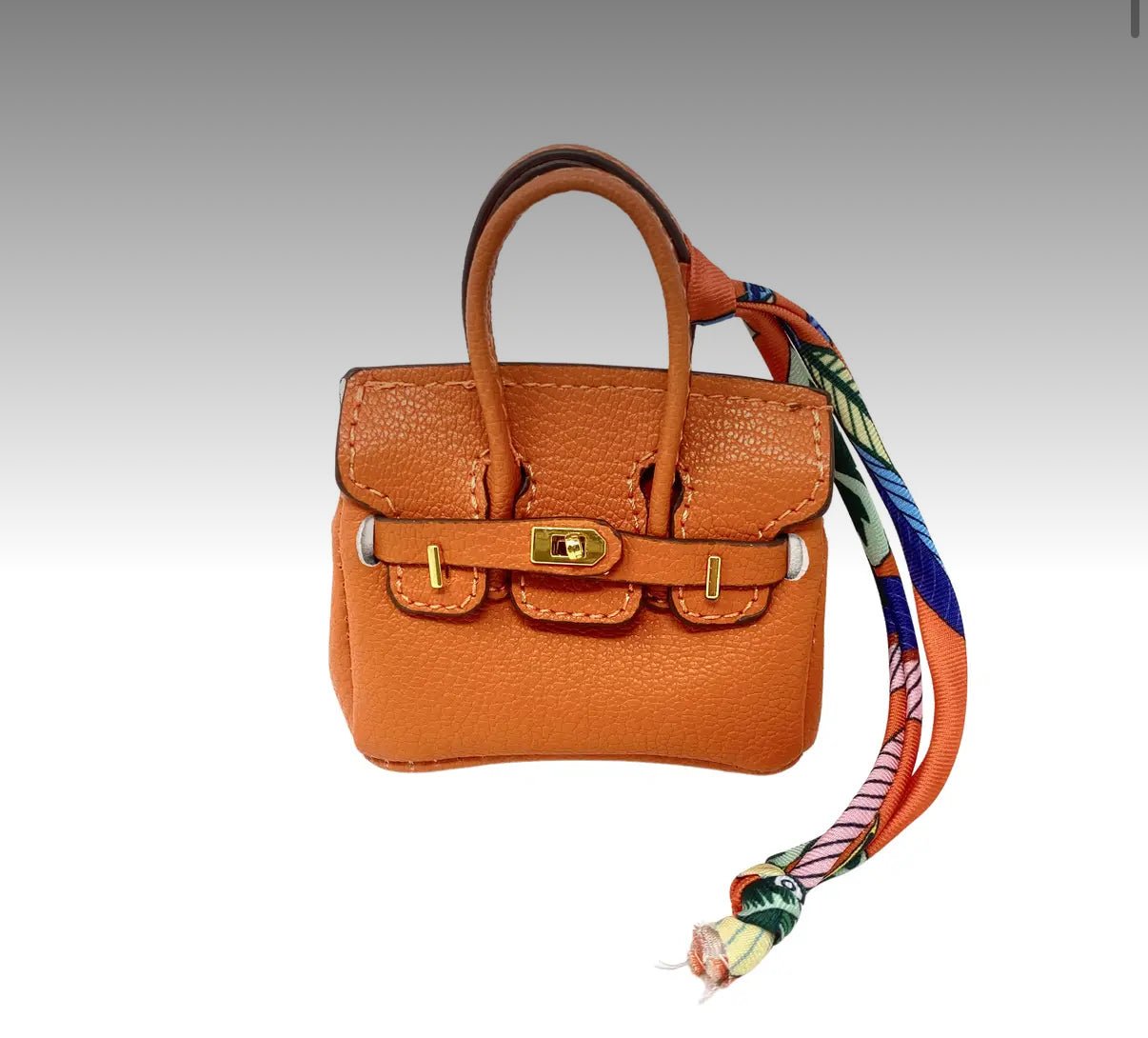 Small brown handbag bag charm with a colorful strap on a light gray background