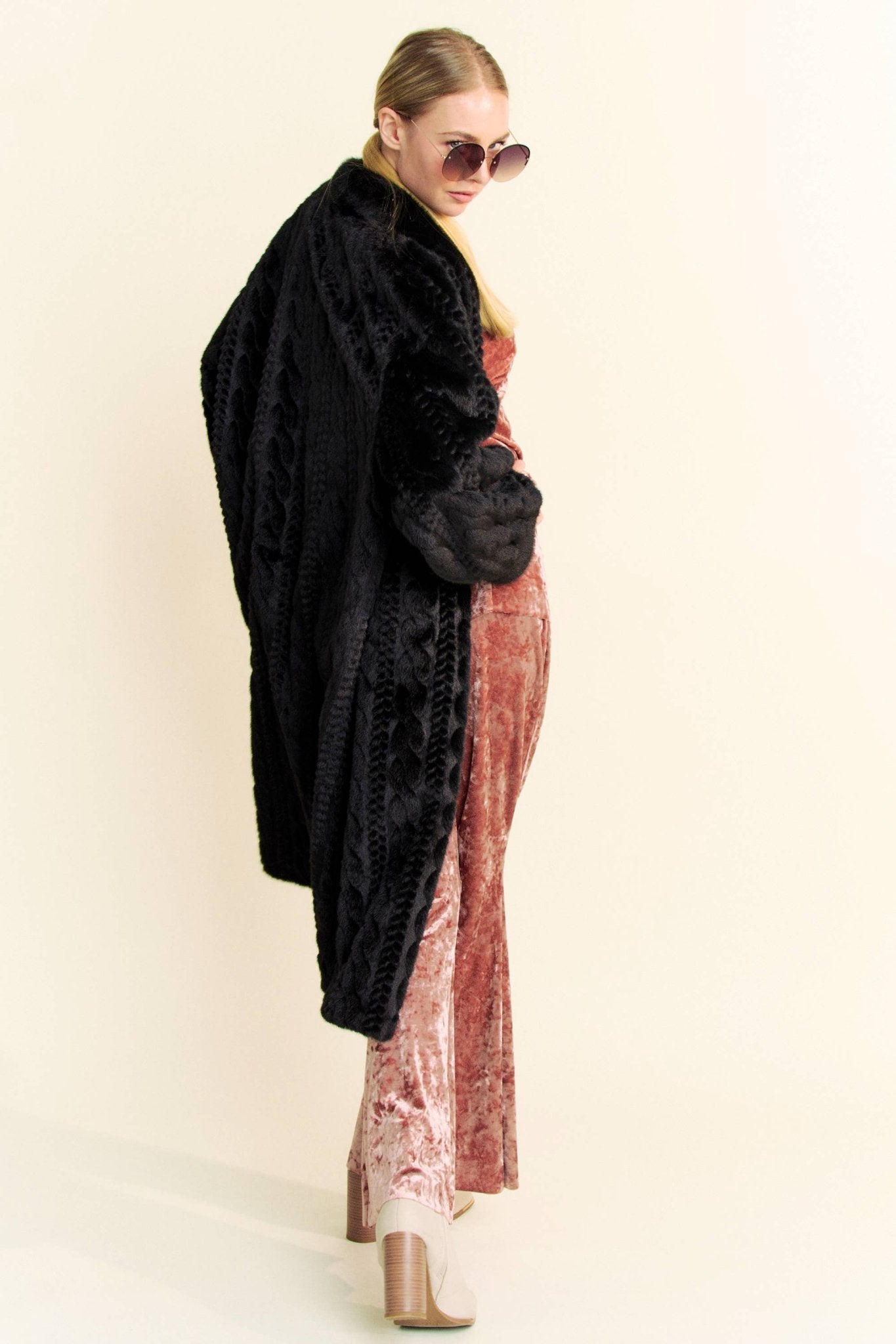 Angled view of a woman wearing a black faux fur coat and round sunglasses