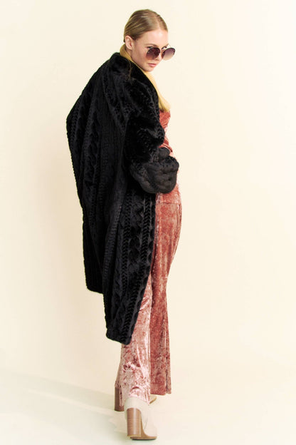 Angled view of a woman wearing a black faux fur coat and round sunglasses