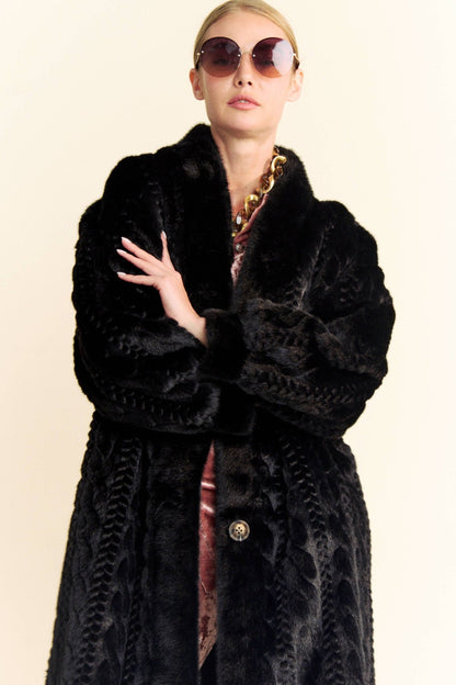 A woman in a black faux fur coat and round sunglasses against a white background