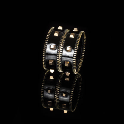 black leather cuff bracelet with gold studded detailing against a black background