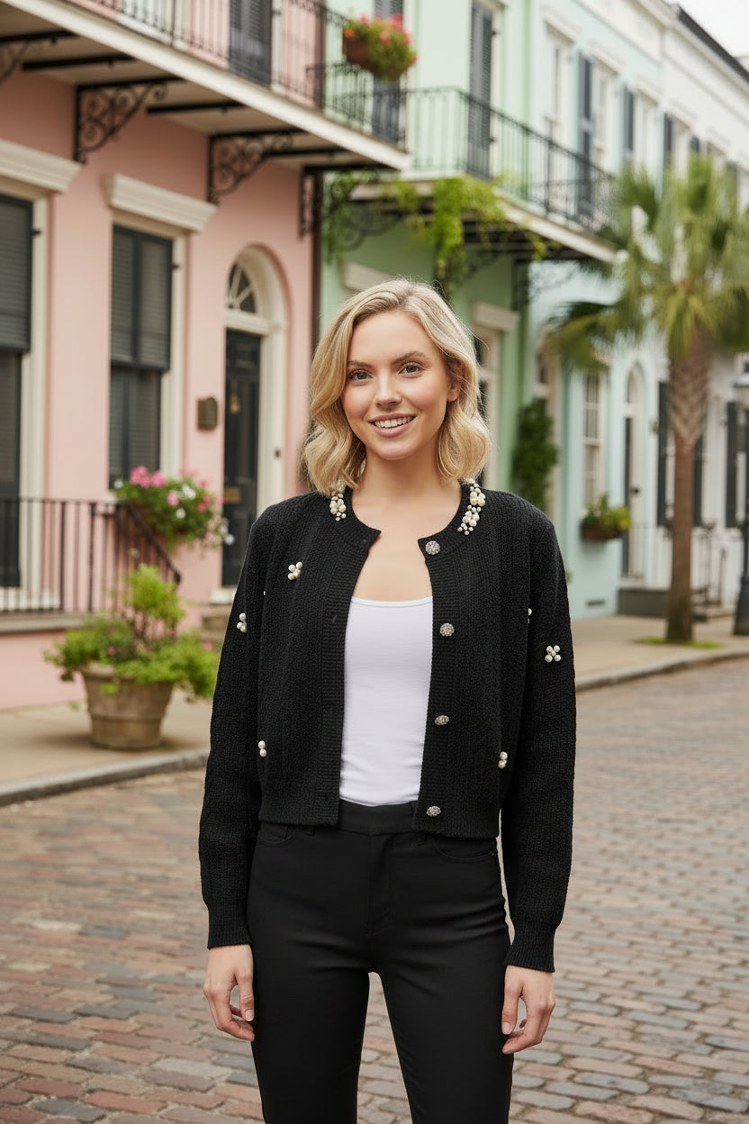 Woman in a black cardigan and black pants standing on a street with colorful houses in the background
