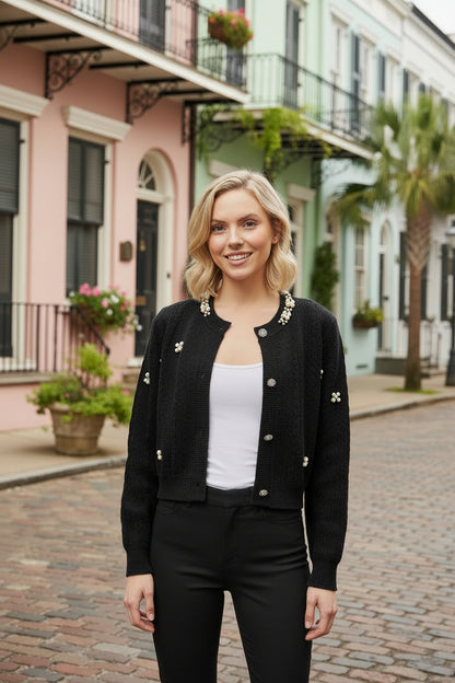 Woman in a black cardigan and black pants standing on a street with colorful houses in the background