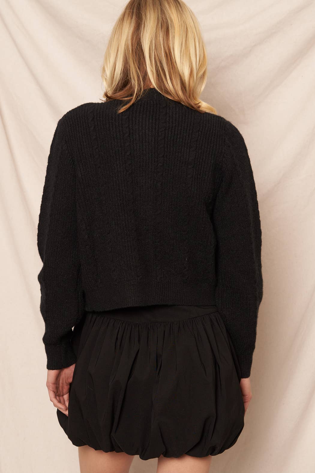 Black view of a woman wearing a black cardigan and black skirt against a neutral background