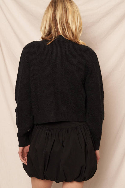 Black view of a woman wearing a black cardigan and black skirt against a neutral background