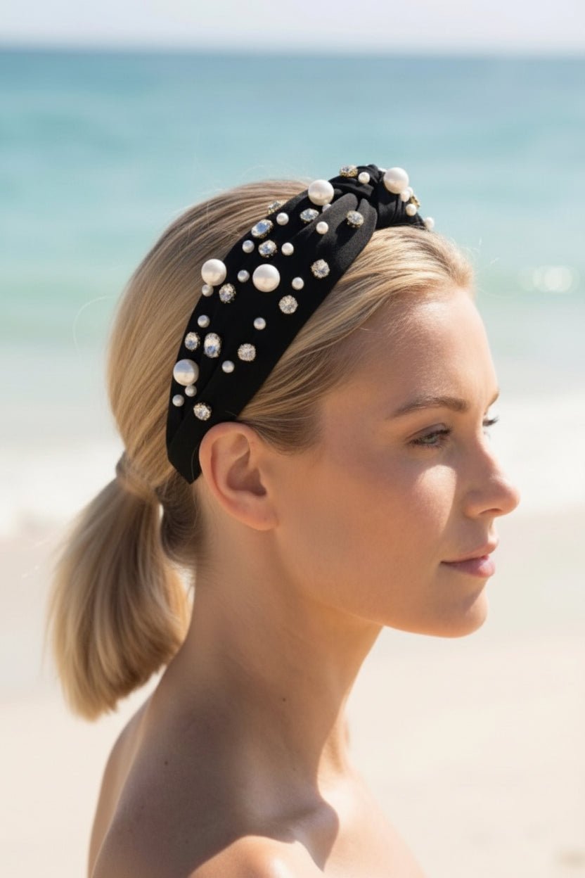 a woman wearing a black pearl and crystal encrusted headband outside with a blurred ocean in the background