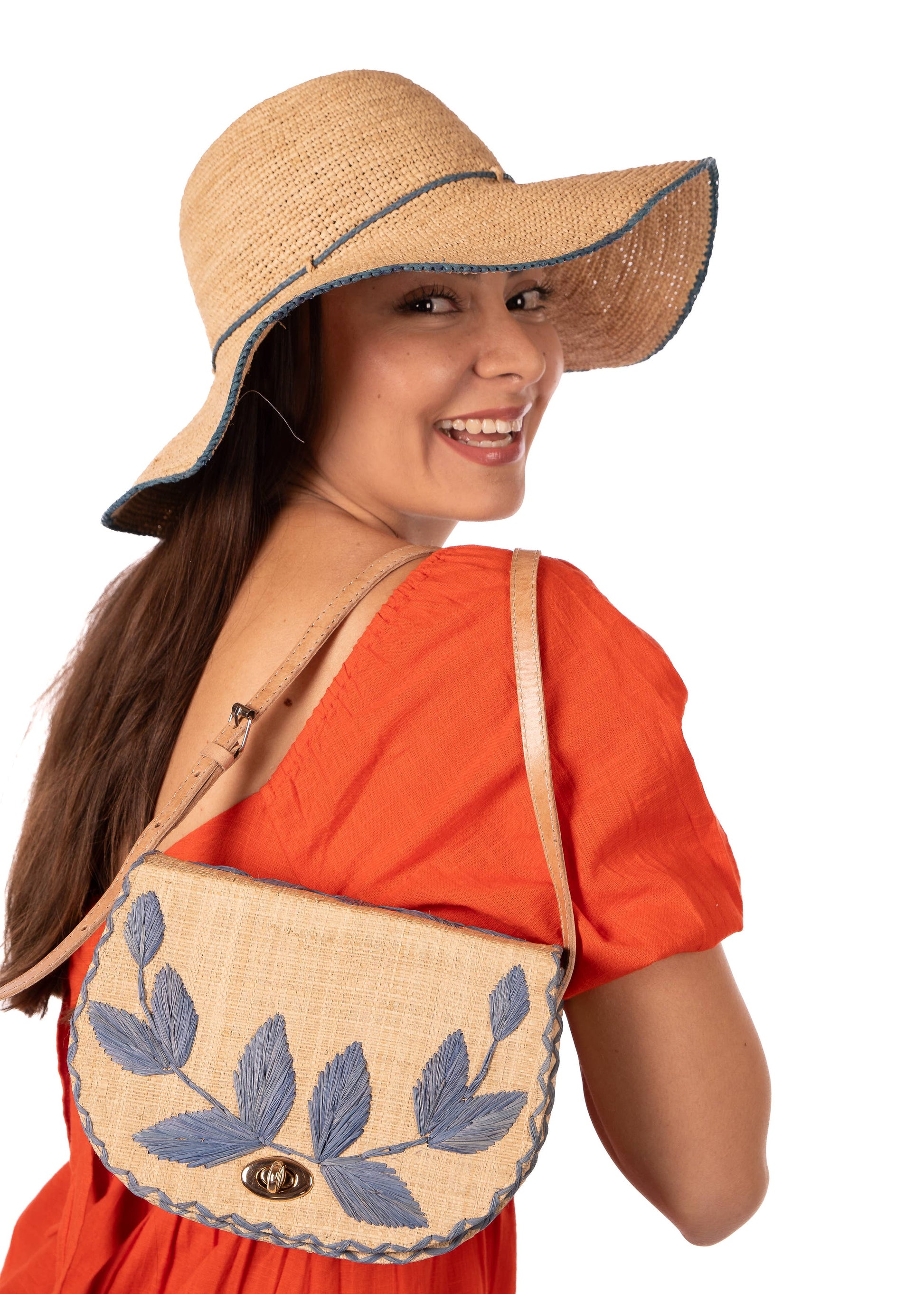 woman holding an embroidered leaf crossbody bag showing adjustable leather strap and structured frame — angled view