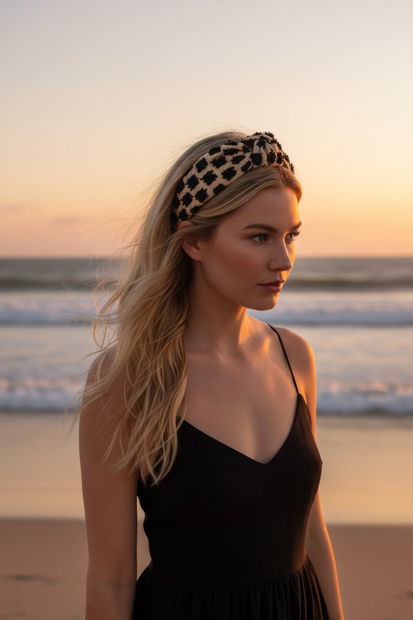 A blonde woman wearing a beige headband with black floral embellishments in an outdoor beach setting