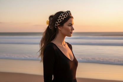 Woman wearing a black dress and black and tan print headband on a beach at sunset.