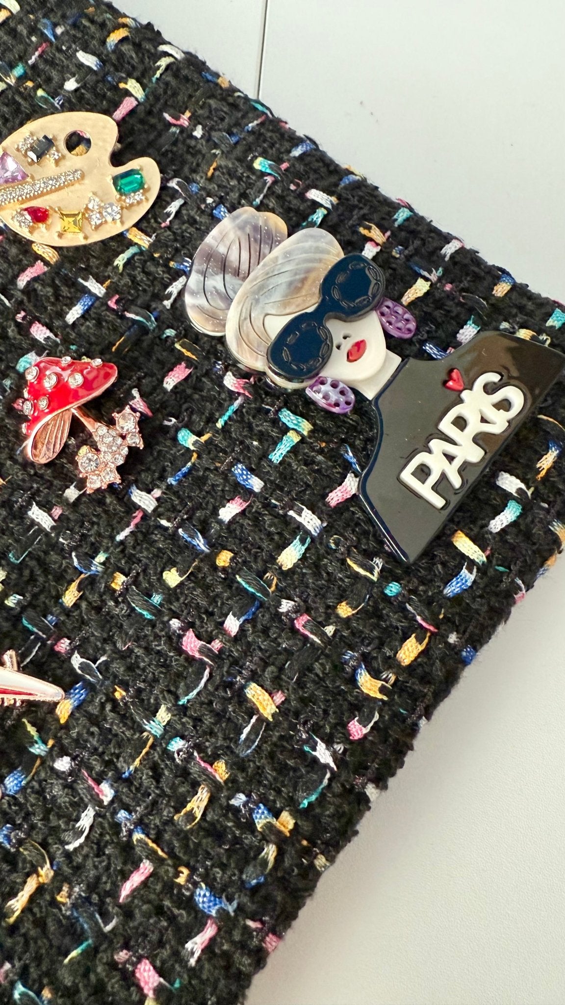 Black textured fabric with colorful brooches and a 'Paris' label.