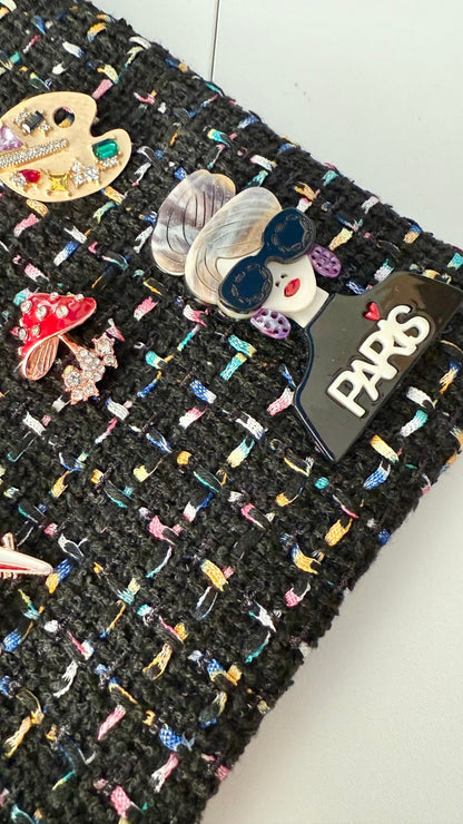 Black textured fabric with colorful brooches and a 'Paris' label.