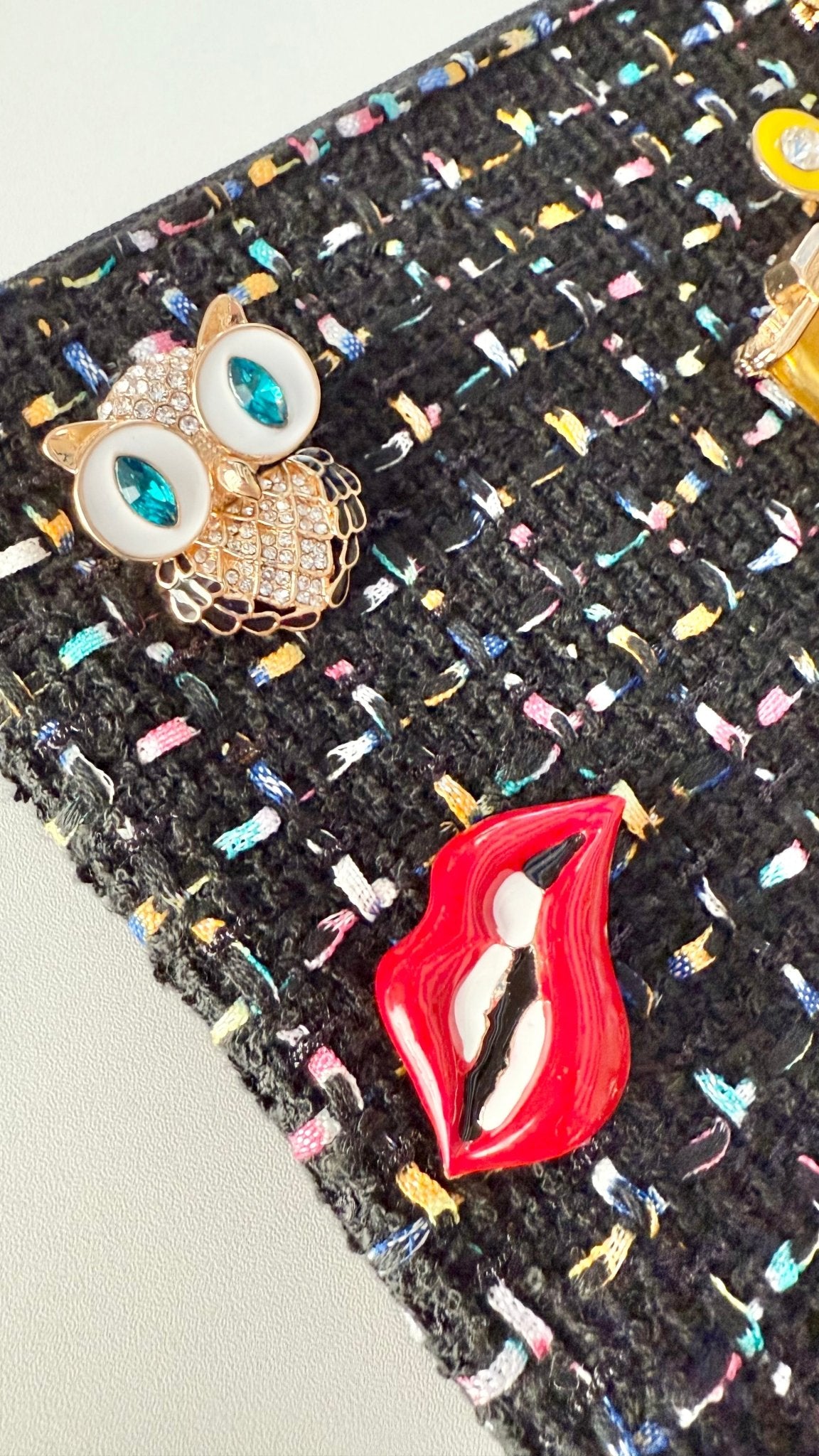 Close-up of a textured surface with an owl brooch and red lips brooch.