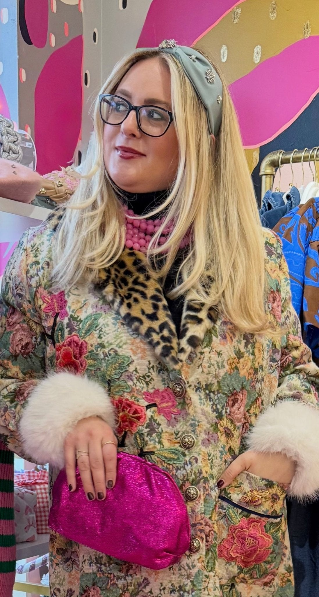 a woman wearing a light blue and crystal headband and floral coat in a boutique store setting