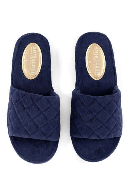 A pair of navy blue terrycloth pool slides with a solid pattern and a quilted design on the strap against a white background