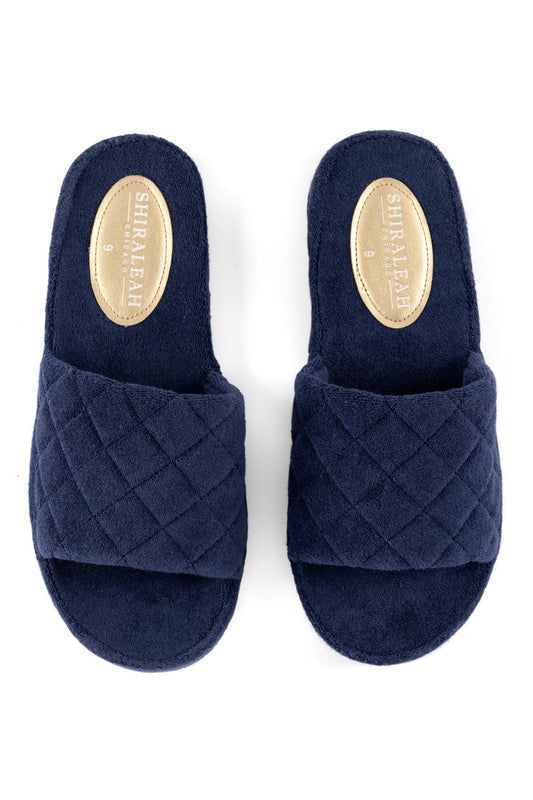 A pair of navy blue terrycloth pool slides with a solid pattern and a quilted design on the strap against a white background
