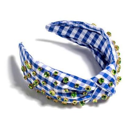 A blue gingham headband with green crystal details laying on a white background