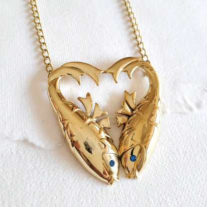 gold double fish heart shaped necklace with inlaid aquamarine stones for the eyes against a white background
