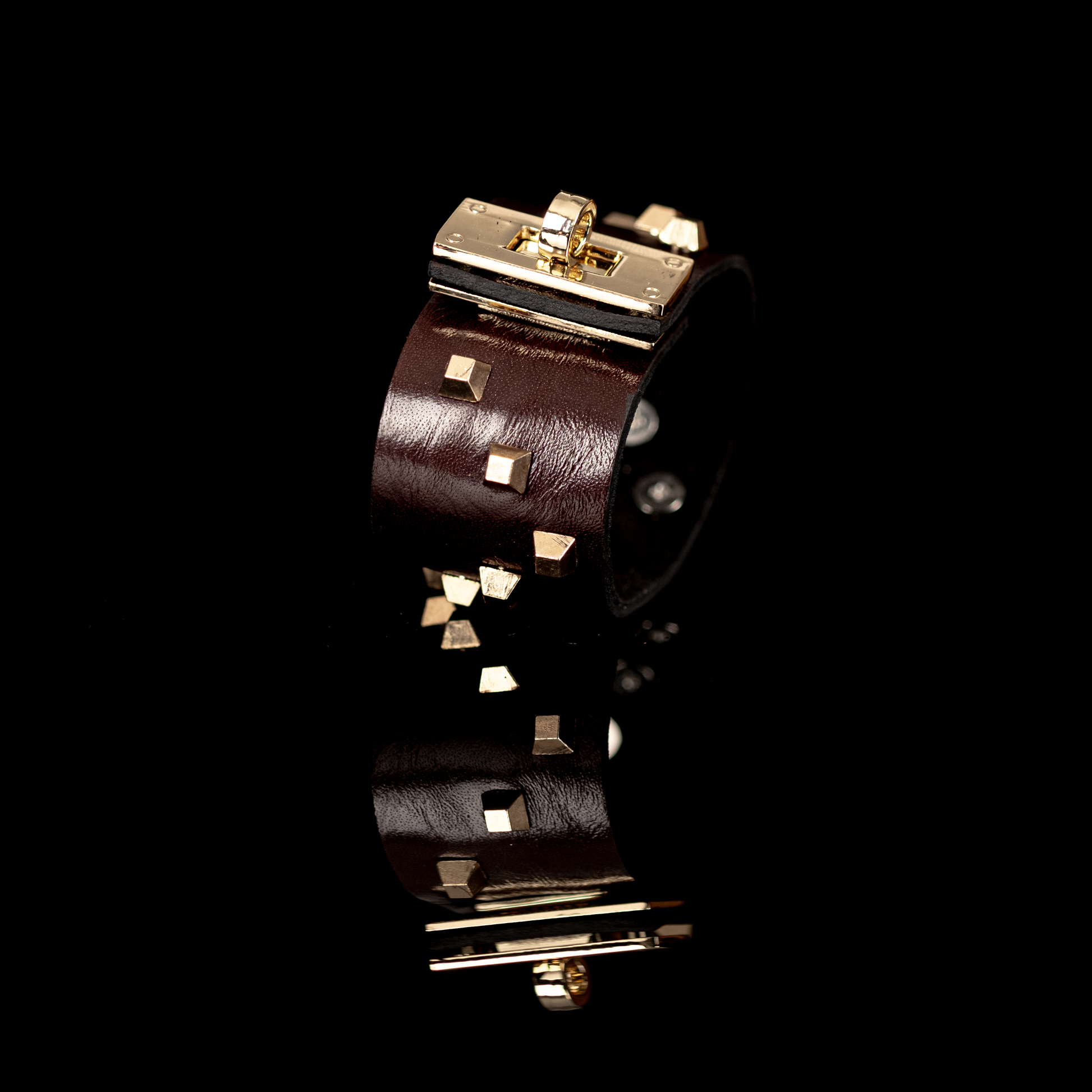 brown leather cuff with gold hardware against a black background