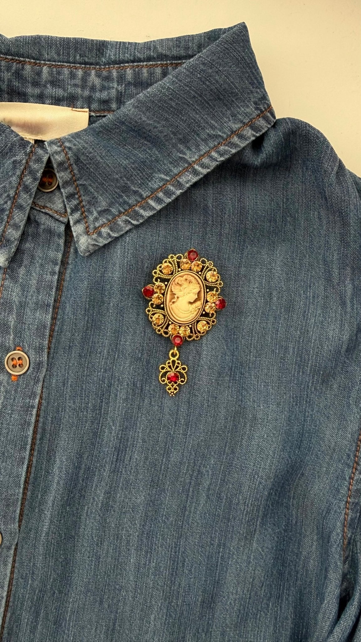 Vintage-style brooch with crystals and a center cameo on a denim shirt against a beige background