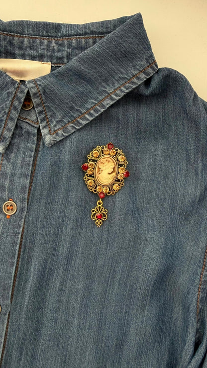 Vintage-style brooch with crystals and a center cameo on a denim shirt against a beige background