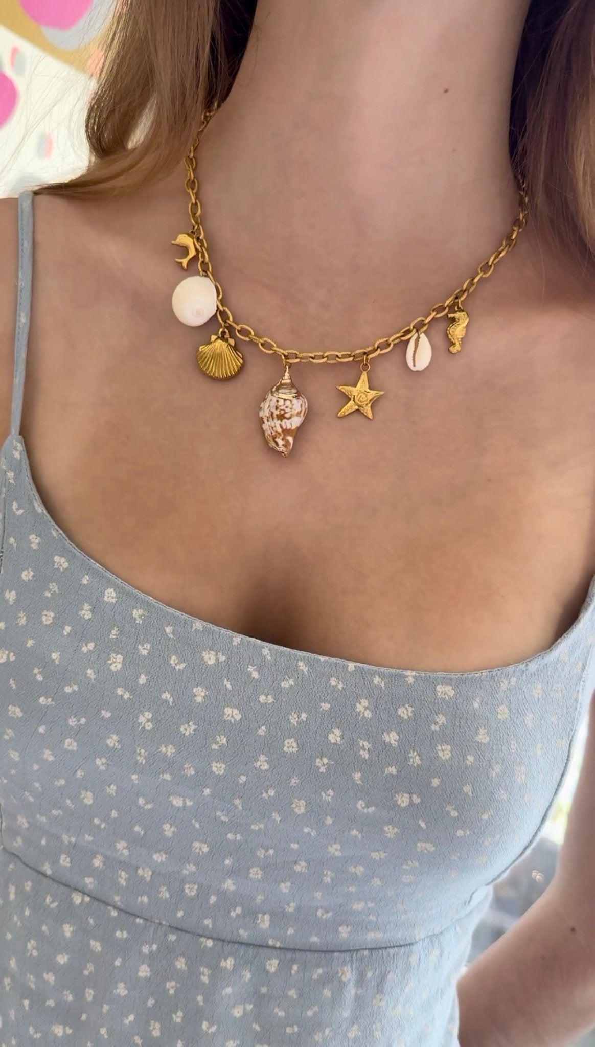 Gold necklace with ocean themed charms worn by a person in a light blue top.